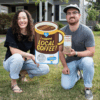 image of a young couple squatting down next to their yard sign that says I support local coffee. the man is holding a bag of coffee from broadway roasters