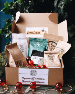 box of a variety of sample bags of coffee beans from kc local roasters. holiday decorations in the background